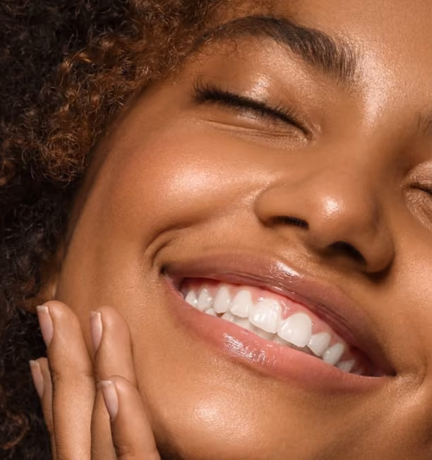 Close-up of a smiling woman with closed eyes and curly hair touching her cheek.