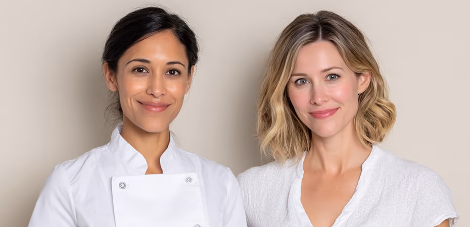 Two smiling women standing side by side, one wearing a white chef coat and the other a white blouse.