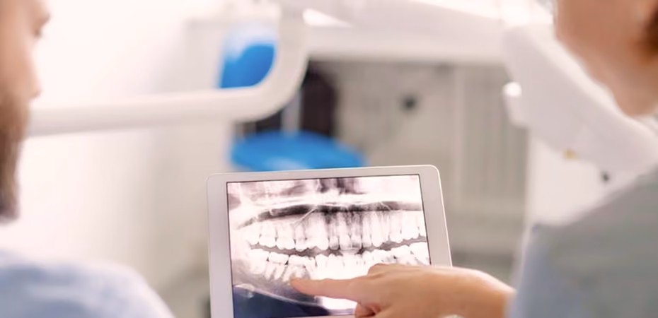 Dentist showing dental X-ray on tablet to a patient in a clinic.